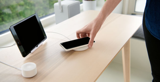 Tabletti sekä kännykkä pöydällä, kännykkä ollaan asettamassa langattomaan laturiin