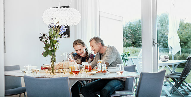Kuva: mies ja nainen katsovat iloisena yhdessä kännykkää aamupalapöydän äärellä