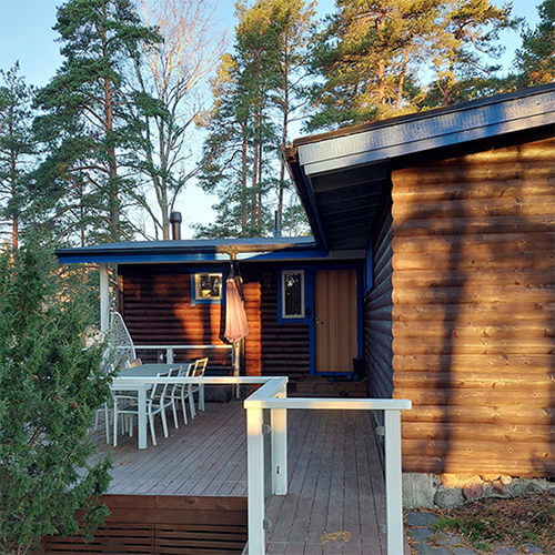 Kuva mökin kulmasta ja ulkopuolelta, jossa näkyy myös mökin terassi