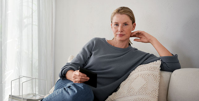 Nainen istuu rennossa asennossa sohvalla, katse kohti kameraa