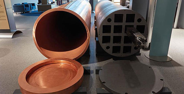 Kaksi kapselia ydinjätteen säilöntään, sylinterimalliset putket joista toinen oranssi ja toinen musta