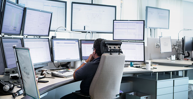 Takaapäin kuvattu henkilö hyvin monen tietokoneruudun äärellä