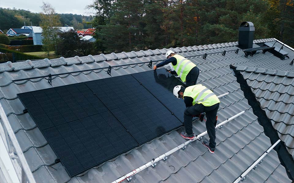 Kaksi asentajaa asentamassa aurinkopaneeleja katolla.