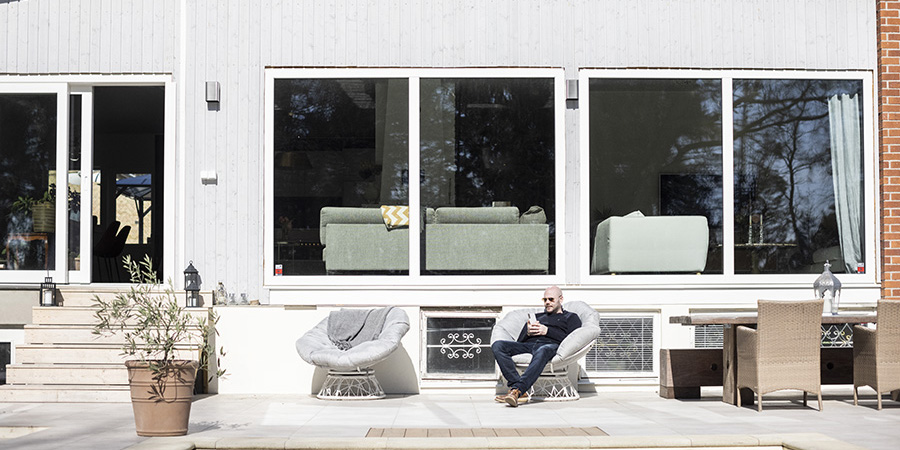 Laaja näkymä ekotalon ulkoterassilta, mies istuu terassin tuolilla aurinkolasit päässä