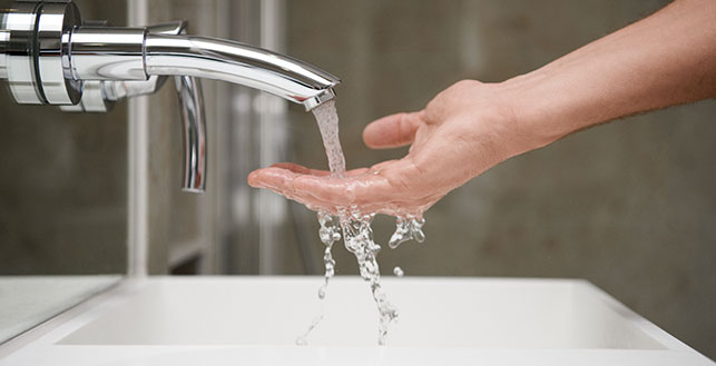 Käsi hanasta tulevan juoksevan veden alla