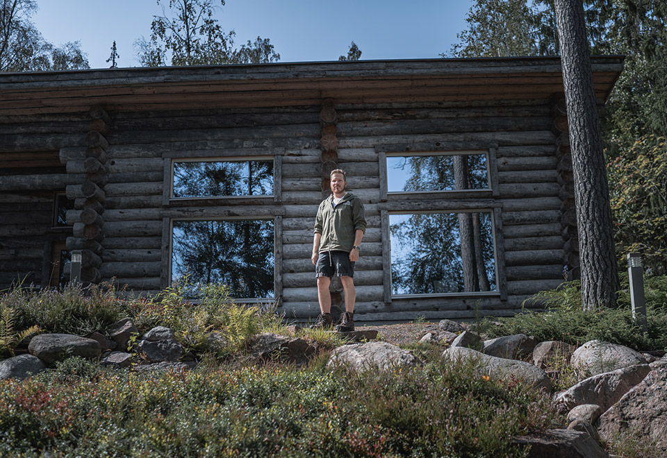 Matti Ala-Outinen hirsimökin edustalla, ympärillä metsää