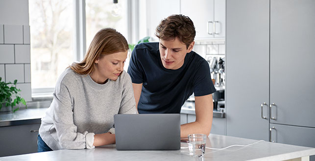 Nainen ja mies keittiössä läppärin äärellä