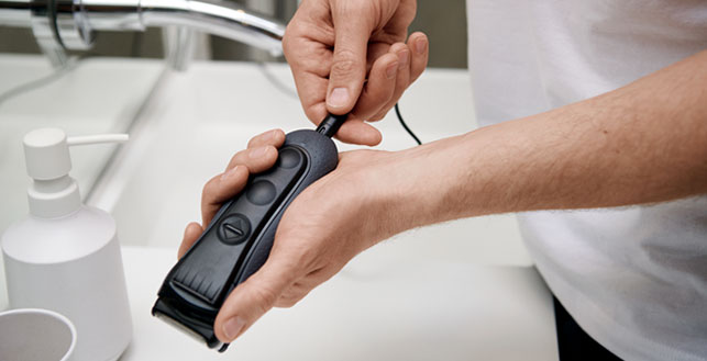 Henkilö asettaa johtoa trimmeriin