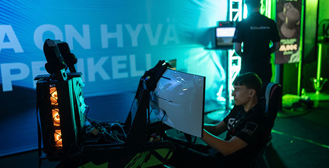 Hämärästi valaistulla tapahtuma-alueella pelaaja tietokoneen äärellä