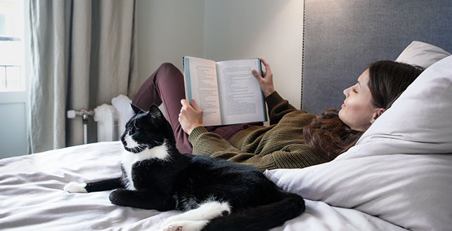 Nainen lukemassa sängyllä kissan vieressä
