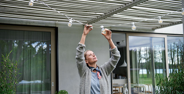 Nainen asettelee ulkoterassin katokseen valonauhaa