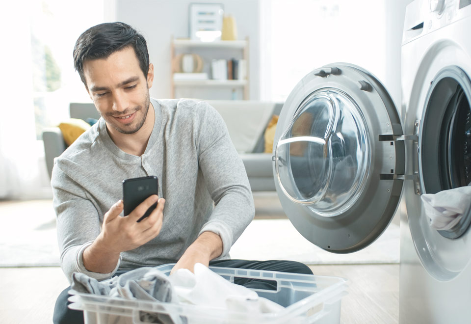Mies pyykkikoneen vieressä katsoo kännykkää