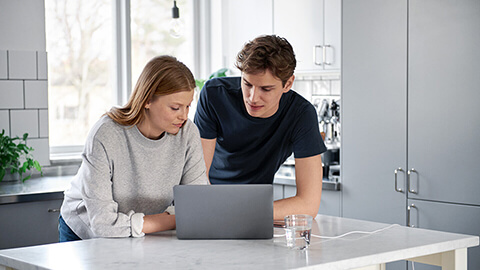 Nainen ja mies katsovat tietokoneen näyttöä keittiössä.