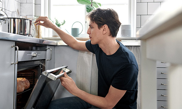 Mies sivulta kuvattuna avaa uunin luukkua