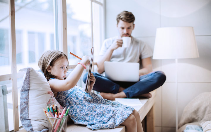 Mies läppärin äärellä ja etualalla lapsi istuu ja piirtää