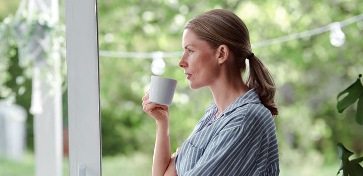 Nainen juo kahvikupista ja katsoo ulos ikkunasta.