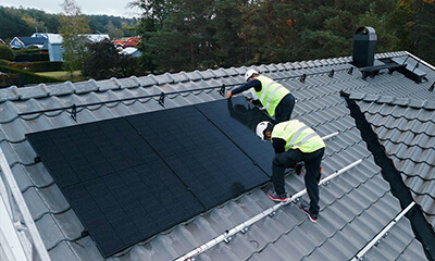 Kaksi asentajaa asentaa aurinkopaneeleja katolla