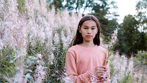 Tyttö pinkissä paidassa vaaleanpunaisten kukkien keskellä.