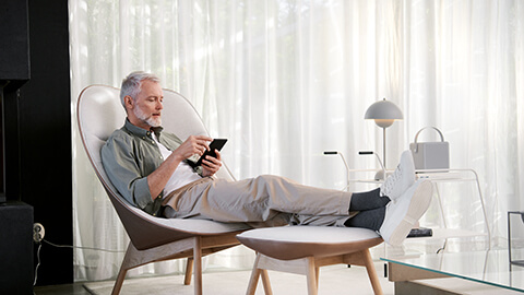 Mies istumassa tuolilla ja selaamassa puhelinta.