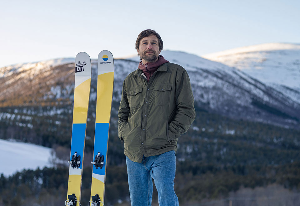 Mies vuoristomaisemassa, vieressään sukset.