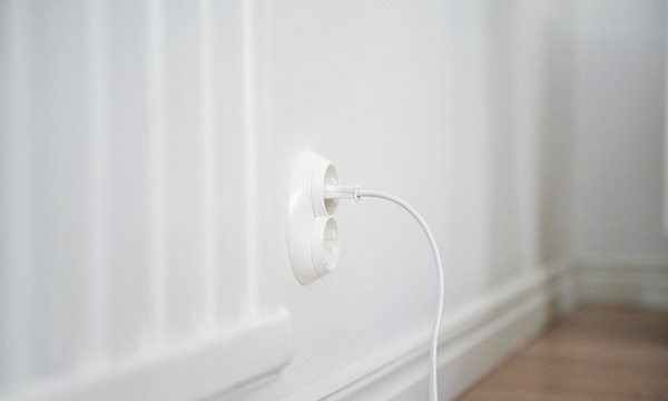 Lähikuva valkoisesta seinästä jonka pistorasiaan on kytketty sähköjohto