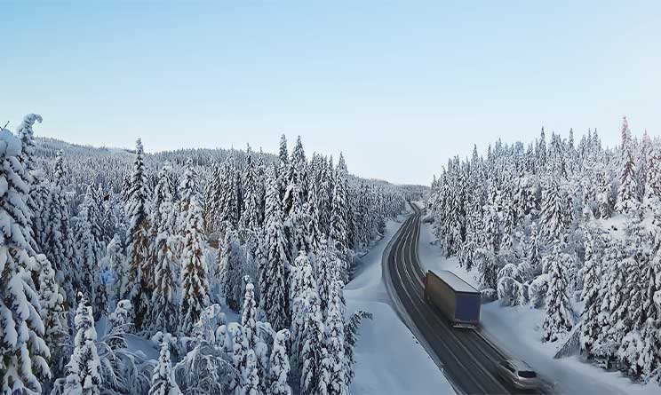 Kaksi ajoneuvoa ajaa tietä pitkin lumipeitteisen metsän halki