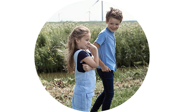 Kaksi lasta pellolla, tuulivoimalla kaukana taustalla