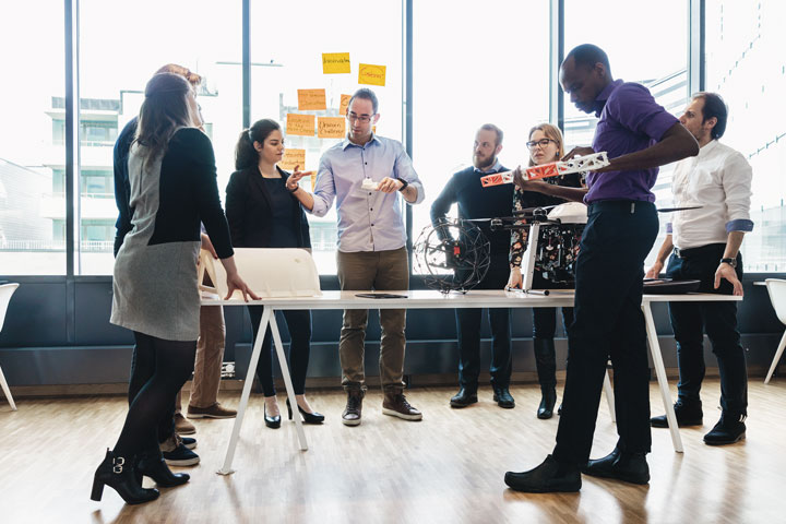 Porukka työntekijöitä seisoo toimiston pöydän ympärillä suunnittelemassa