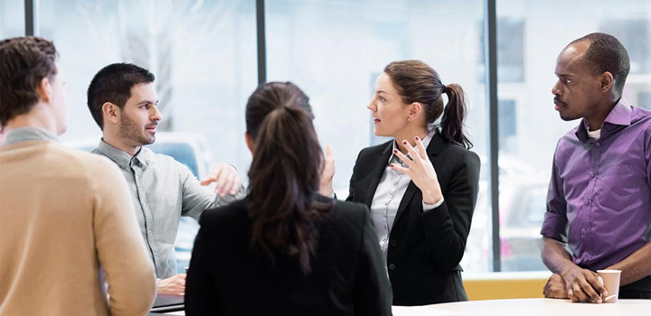 Viisi henkilöä pöydän ympärillä toimistossa keskustelemassa