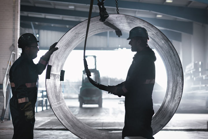 Kahden työmiehen tumma silluetti vasten tehdasympäristöä