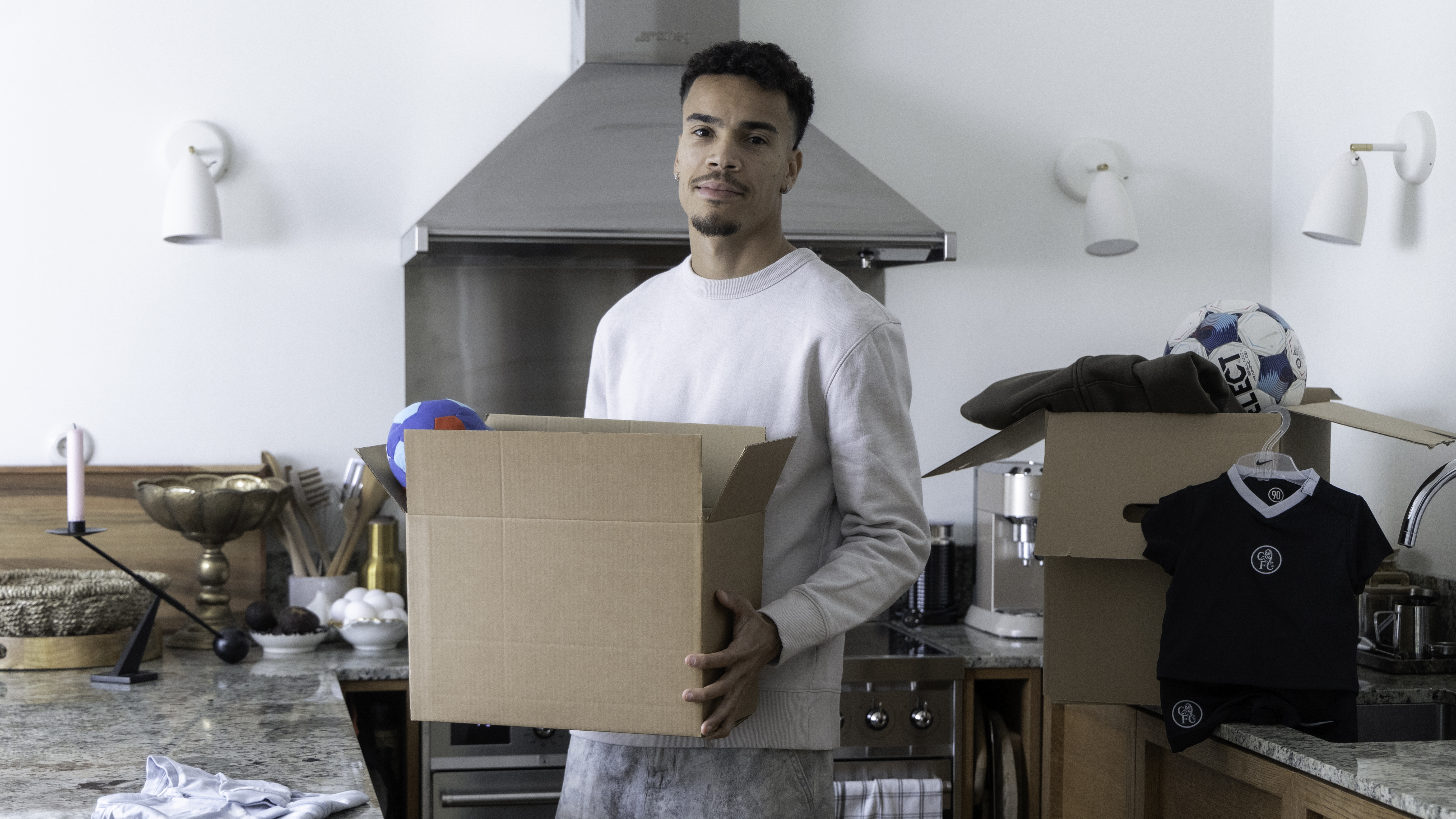 Pyry soiri seisoo keittiössä muuttolaatikko sylissä, ympärillään muuttotavaraa pitkin keittiön pöytää